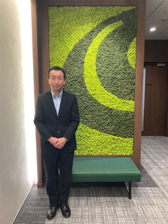 鈴木さん(会社ロゴをイメージした藻の装飾前で)