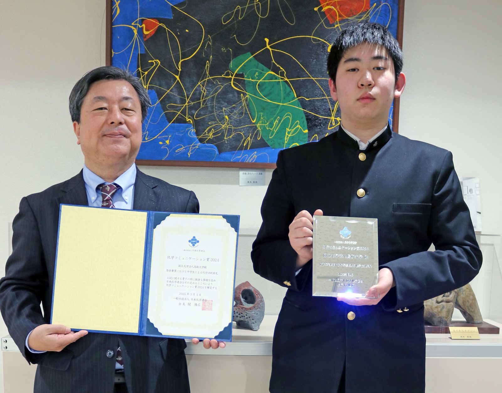 化学コミュニケーション賞の賞状を持つ片田先生(左)と、受賞記念の盾を持つ田村さん(右) 化学コミュニケーション賞の賞状を持つ片田先生(左)と、受賞記念の盾を持つ田村さん(右)